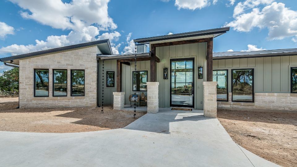  An Allen single family home is pictured with a modern, gray exterior with light brick and an angled roof, against a blue and cloudy sky.